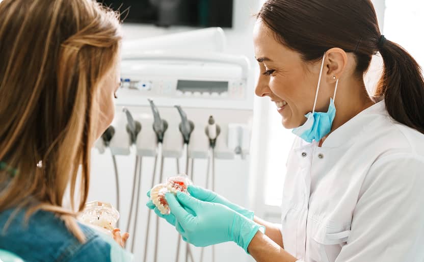 North End Dental | Dentist smiling while showing a young patient a dental model during a consultation